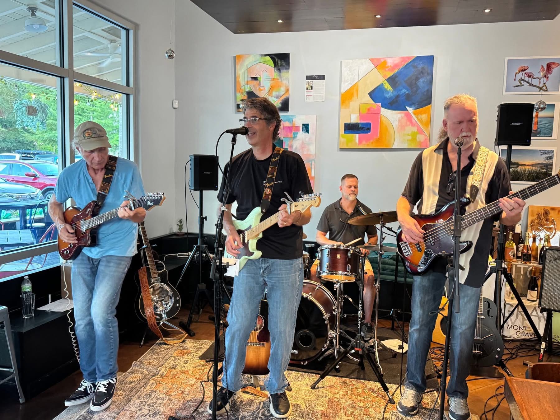 The band playing an indoor show, guitars and drums in front of colorful paintings