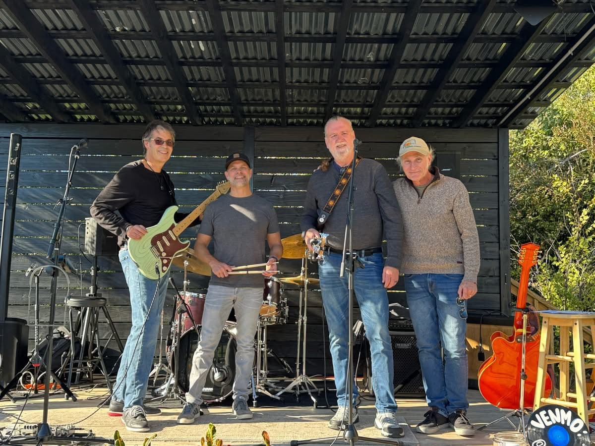 The band standing on an outdoor wooden stage with their instruments